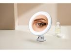 Oglindă de toaletă iluminată cu ventuză pe o suprafață albă lângă dischete demachiante și parfum.