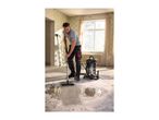 Man using a wet and dry vacuum cleaner to clean a construction site floor.