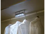 A closet with a motion-activated LED light illuminating three white dress shirts hanging on wooden hangers.