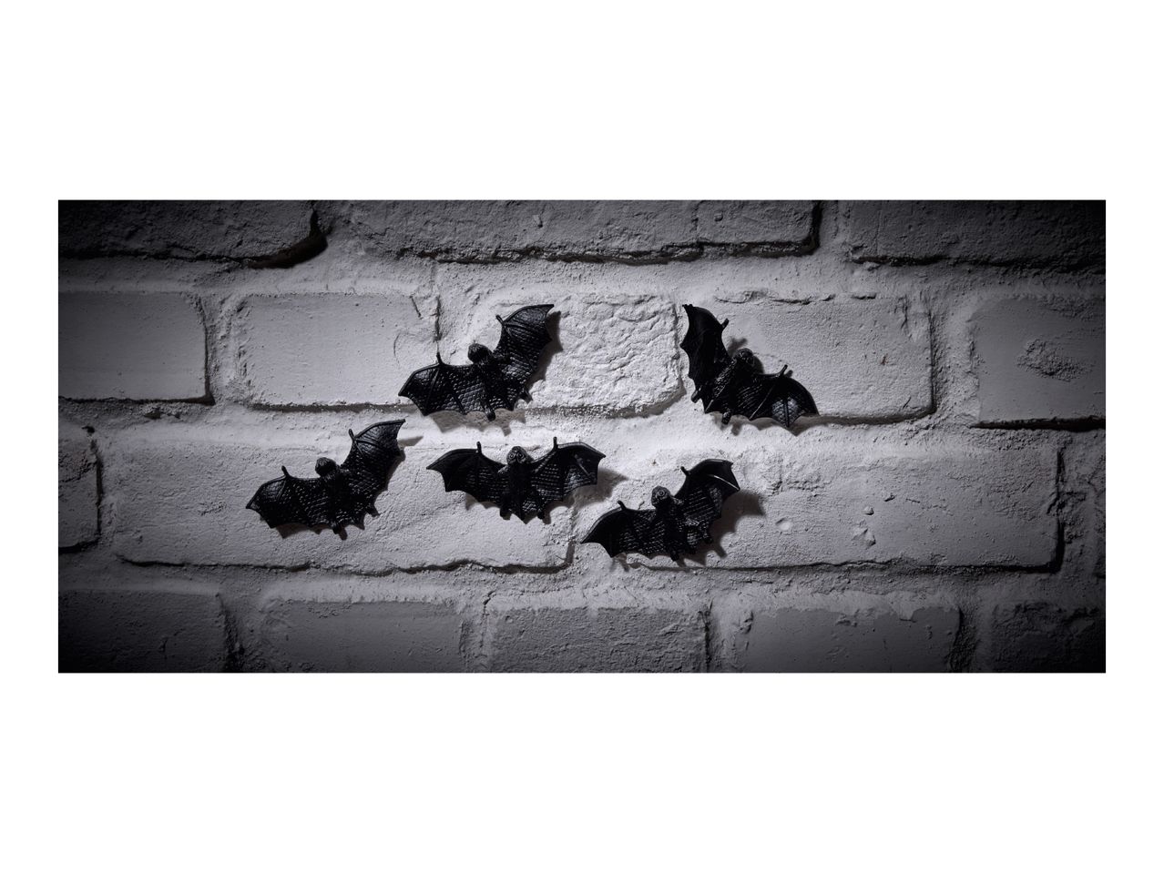 Six black bat decorations on a white brick wall, illuminated by a spotlight.