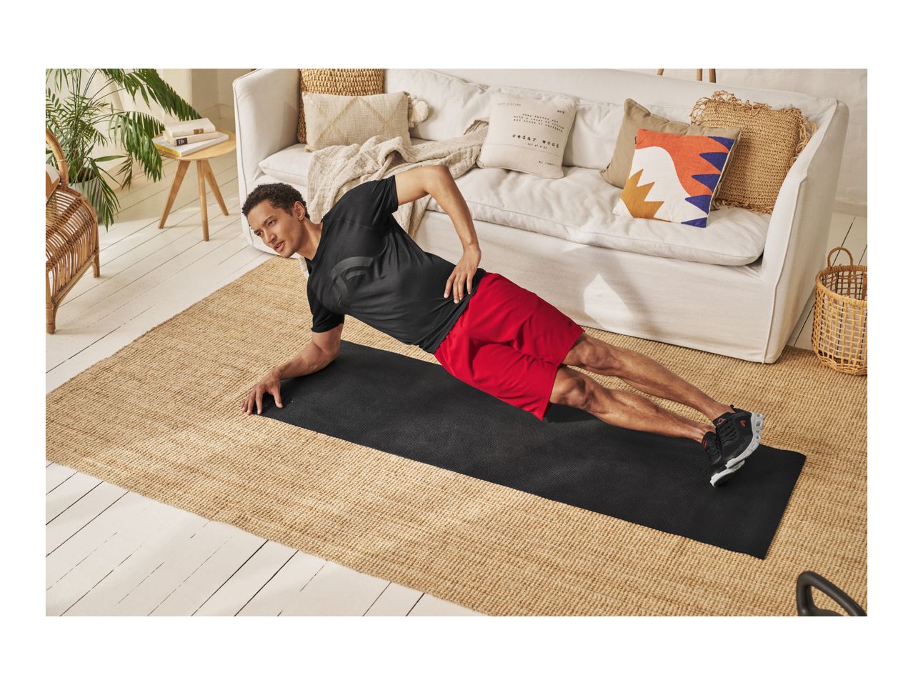 Man in black t-shirt and red shorts doing a side plank on a black exercise mat.