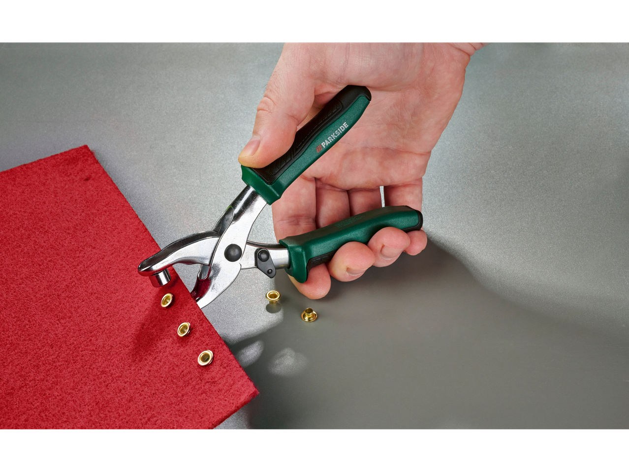 Ruka koristi klešta za nitne na crvenoj tkanini sa mesinganim nitnama