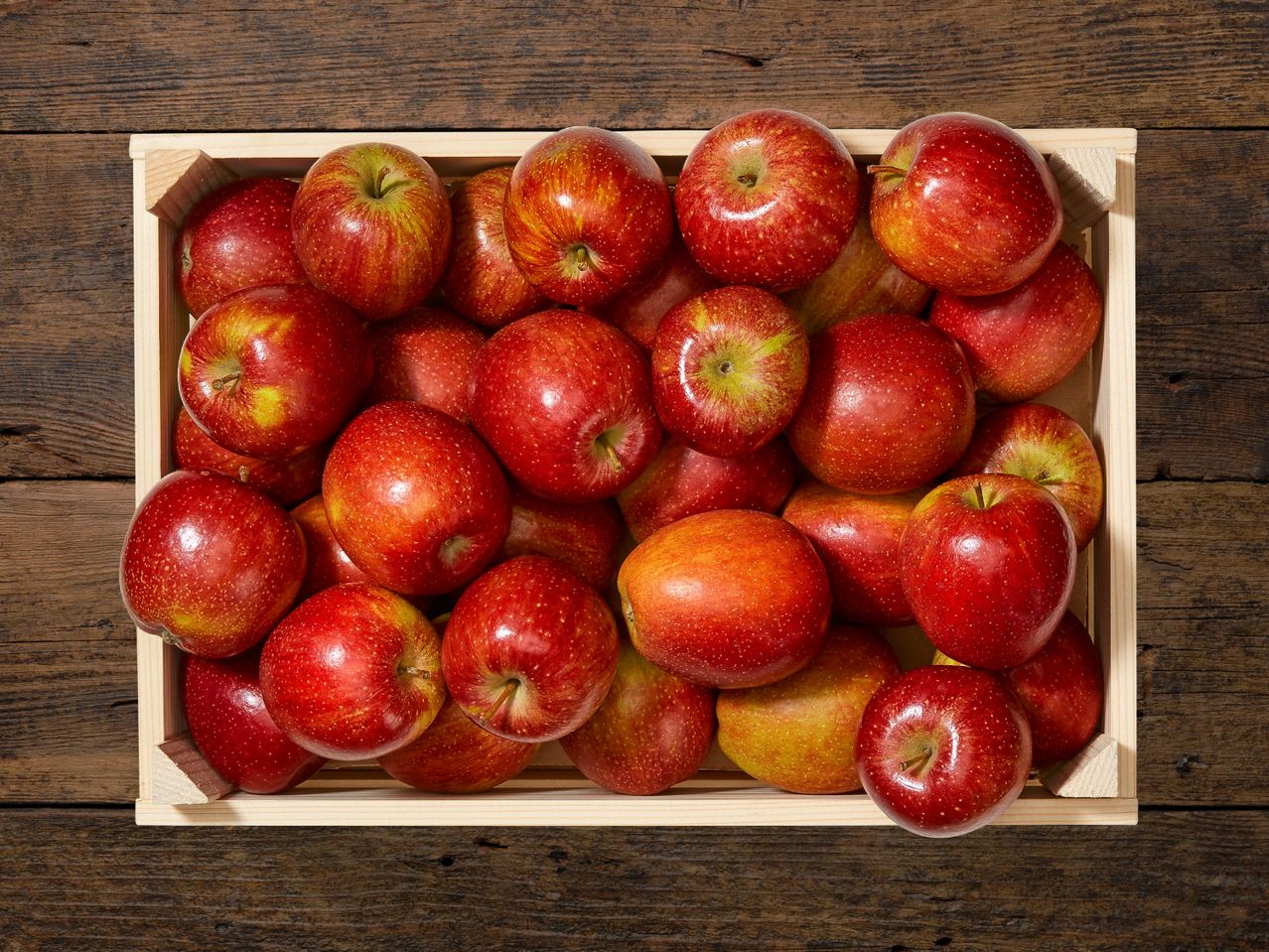 Una cassetta di legno piena di mele rosse succose.