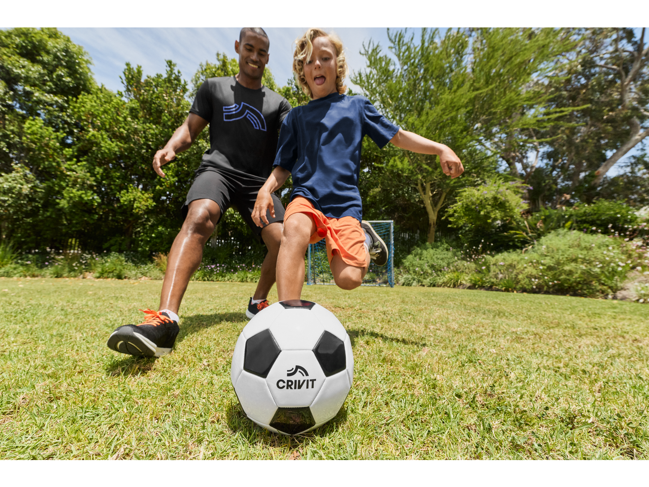 Father and son playing soccer with a CRIVIT ball on a sunny day.