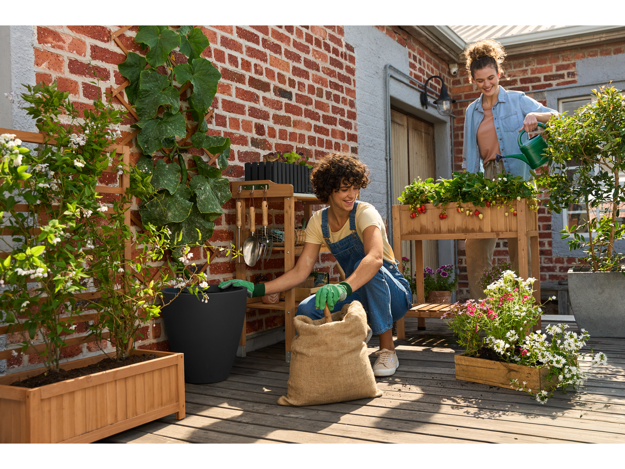 Two women gardening on a patio, one wearing Parkside® Gardening Gloves, planting from a burlap sack.