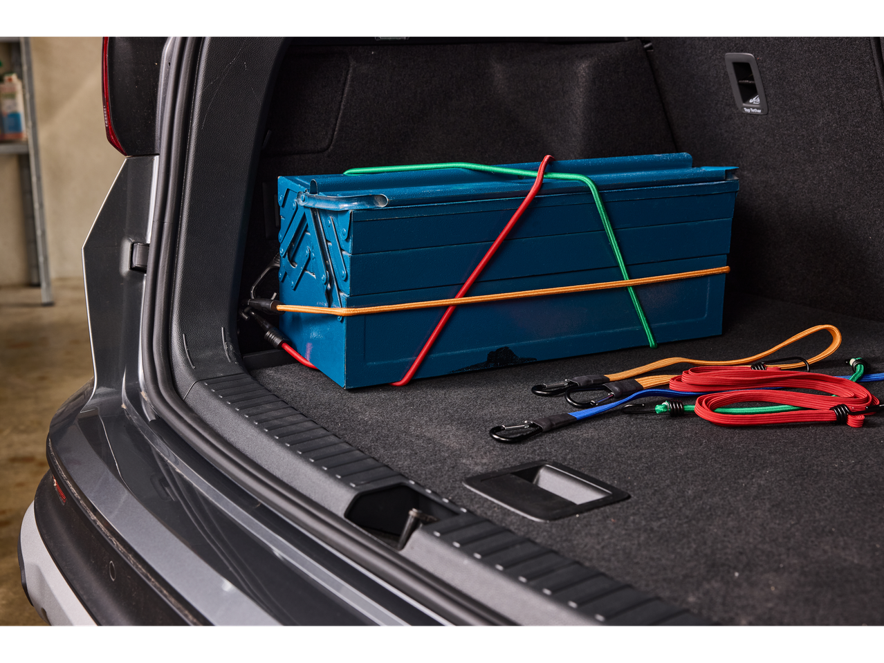 ULTIMATE SPEED® Bungee Cord Set securing a blue toolbox in a car trunk.