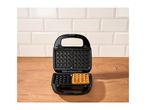 Open waffle maker with one golden waffle on a wooden counter against a tiled wall.