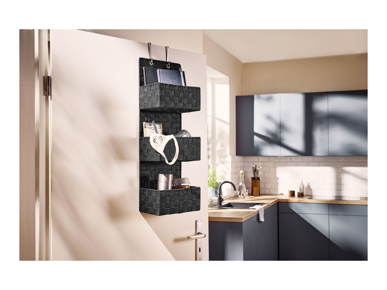 Three-tier dark grey hanging organizer mounted on a door in a kitchen setting.