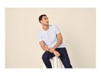 Man in white t-shirt and dark blue trousers sitting on a stool, looking right.