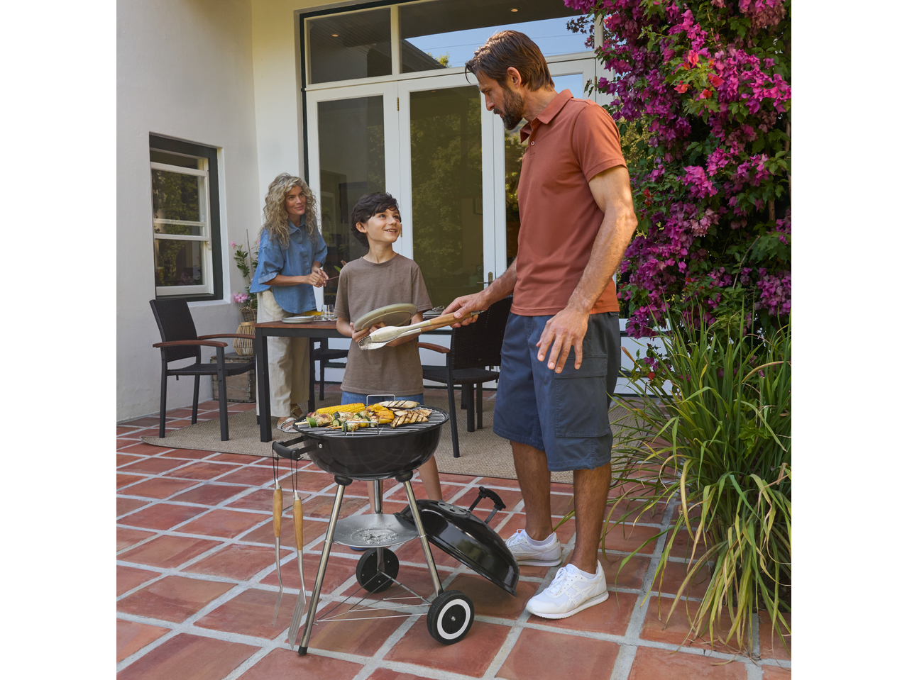 Otac i sin roštiljaju na Kettle Barbecue roštilju, sa majkom u pozadini.