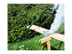 A person using a green bow saw to cut a wooden plank on a sawhorse outdoors.