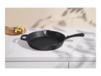 Black cast iron skillet on a white marble countertop with potatoes and garlic.