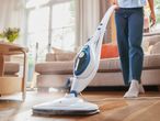 A person uses a steam mop to clean a hardwood floor.