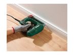 Person using an electric stapler to attach a white baseboard to a wall.