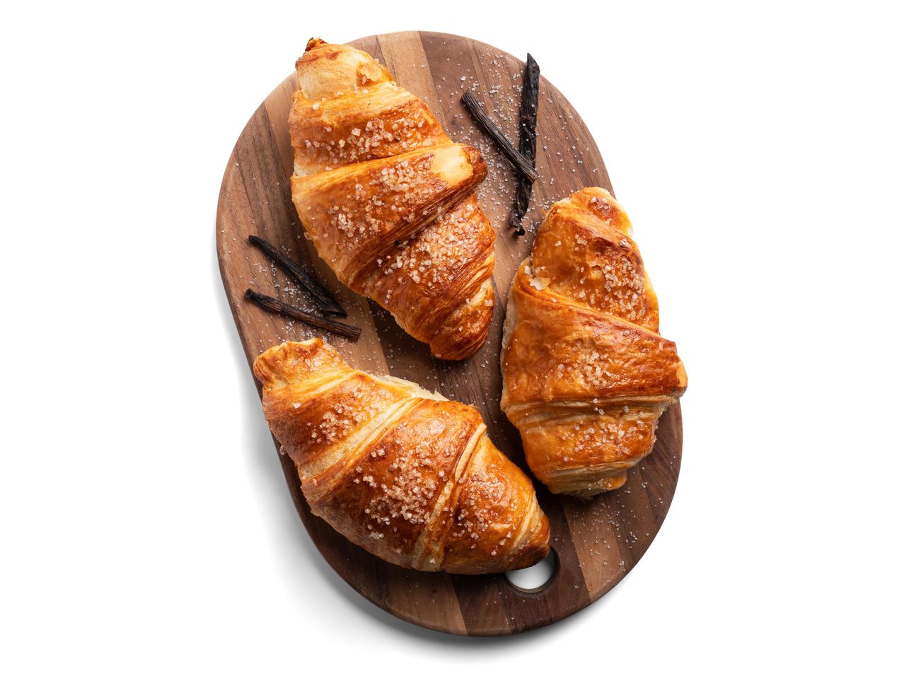Három vaníliás croissant vanília rudakkal és cukorral megszórva egy fa vágódeszkán.