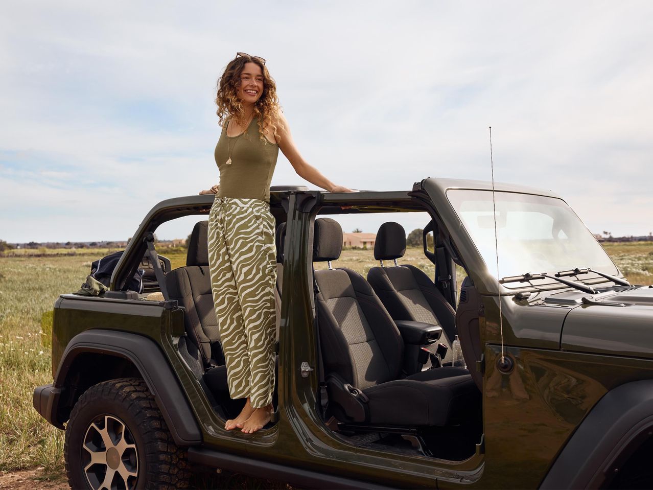 Női modell egy zöld Jeep Wranglerben, virágos midi szoknyában.