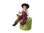 Smiling child in burgundy rain overalls holding a green bucket, sitting on a green cylinder.
