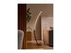 A modern black floor lamp with a curved design illuminates a living room with a beige sofa.