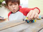 Момче си играе с колички Hot Wheels на маса.