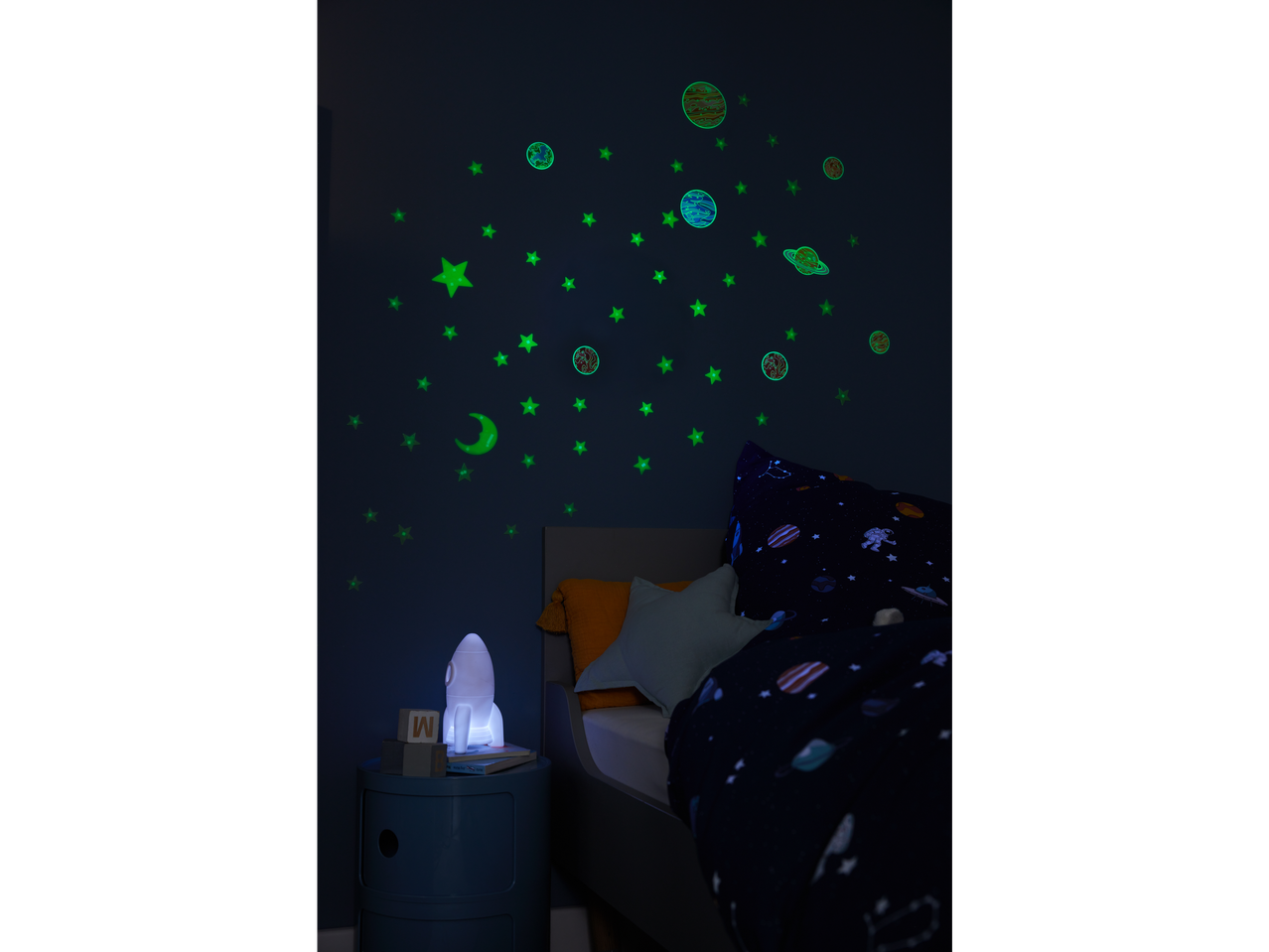 Quarto infantil com adesivos brilhantes no escuro com tema espacial e um abajur em formato de foguete.