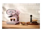Pink espresso machine brewing coffee into two glasses on a wooden counter with cookies and coffee beans.