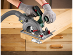 Parkside cordless circular saw cutting a wooden plank on a workbench.