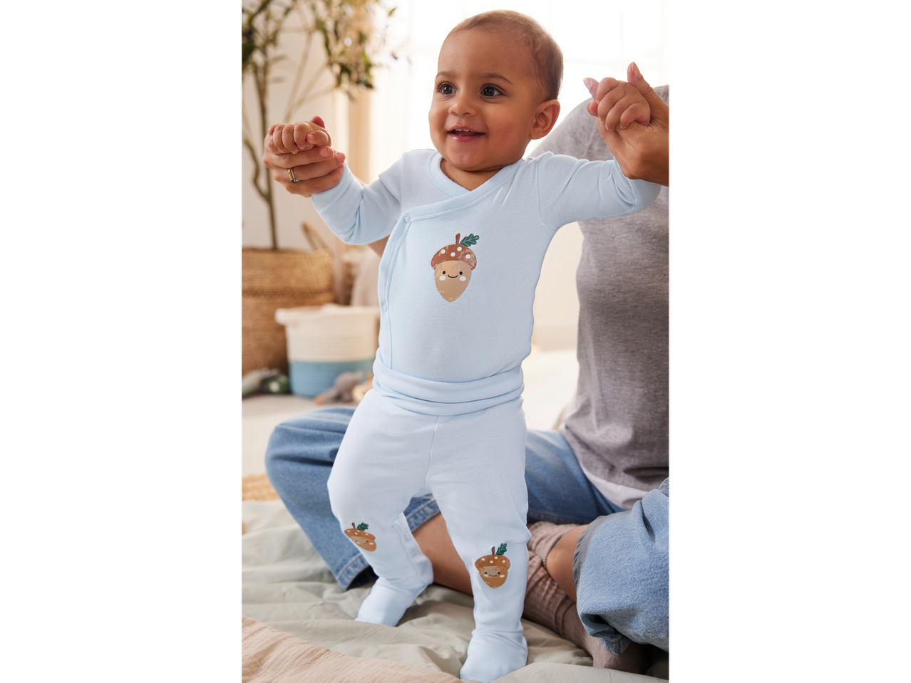 Baby in light blue acorn-themed sleepwear, held by an adult.