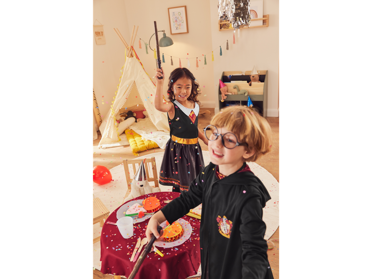 Two children in Harry Potter costumes playing with wands and confetti.