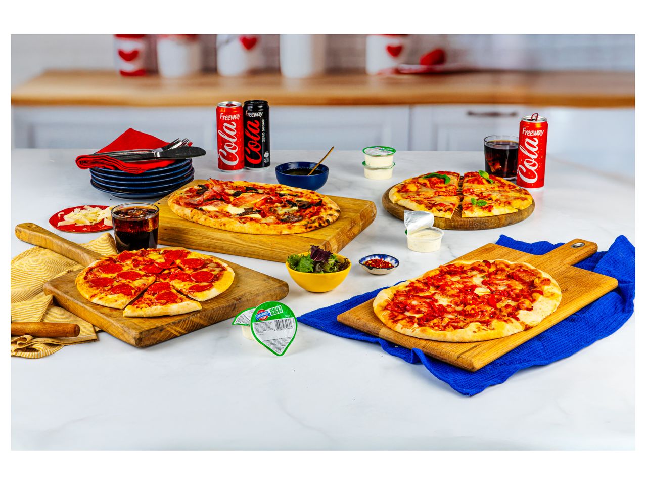 Four small pizzas on wooden boards, with Coca-Cola cans and other food items.