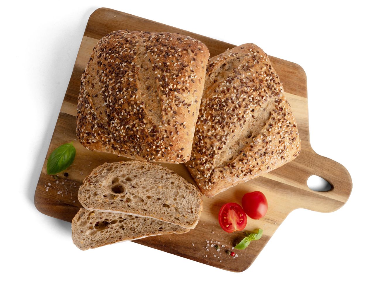 Teljes kiőrlésű kenyér szezámmaggal és lenmaggal, paradicsommal és bazsalikommal egy vágódeszkán.
