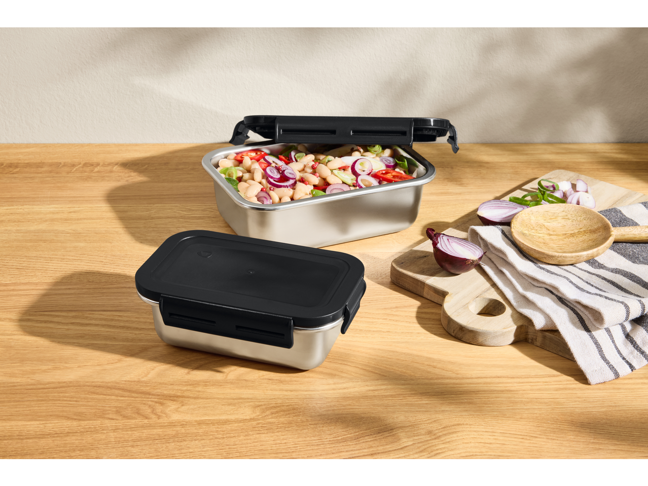 Două recipiente de depozitare din oțel inoxidabil, unul deschis cu salată de fasole, pe o masă de lemn.