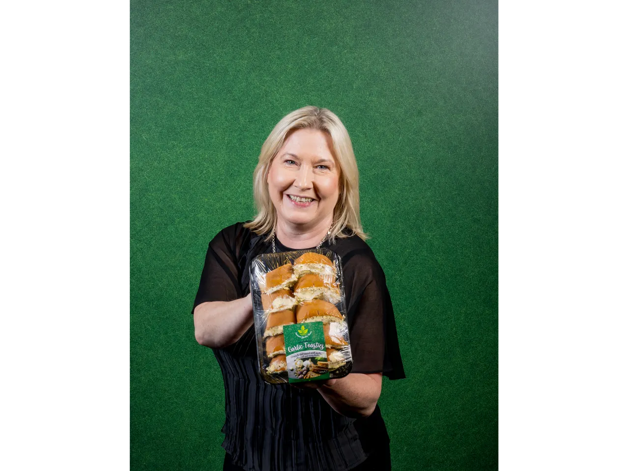 A woman holding a package of garlic toasties against a green background.