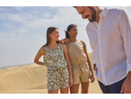 Duas mulheres de macacões e um homem de camisa branca e calças escuras nas dunas de areia.