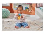 Baby sitting on a rug, holding a colorful toy, with a teal pouf and shelves in the background.