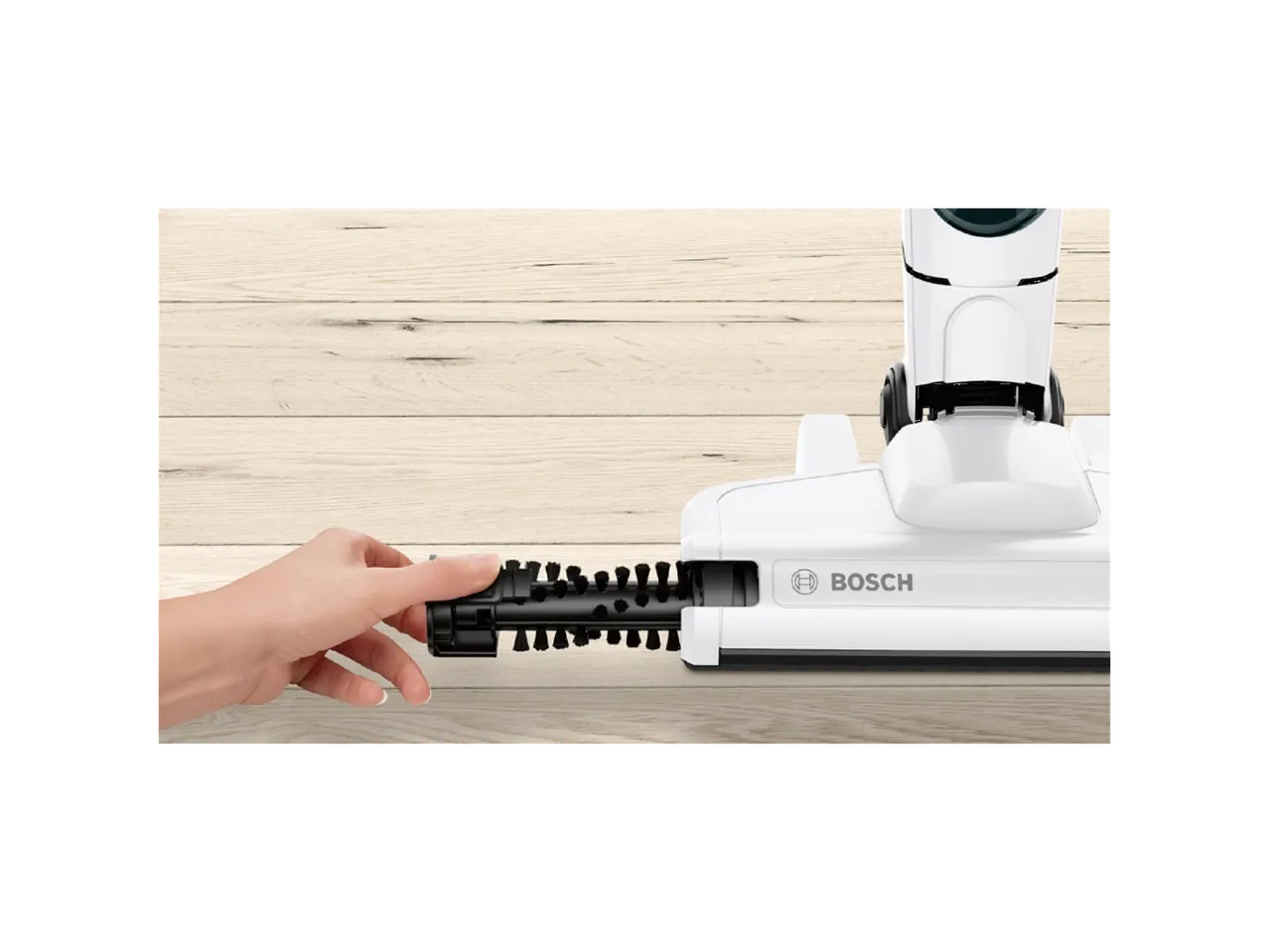 A hand removing the brush roller from a white Bosch cordless vacuum cleaner head on a wooden floor.