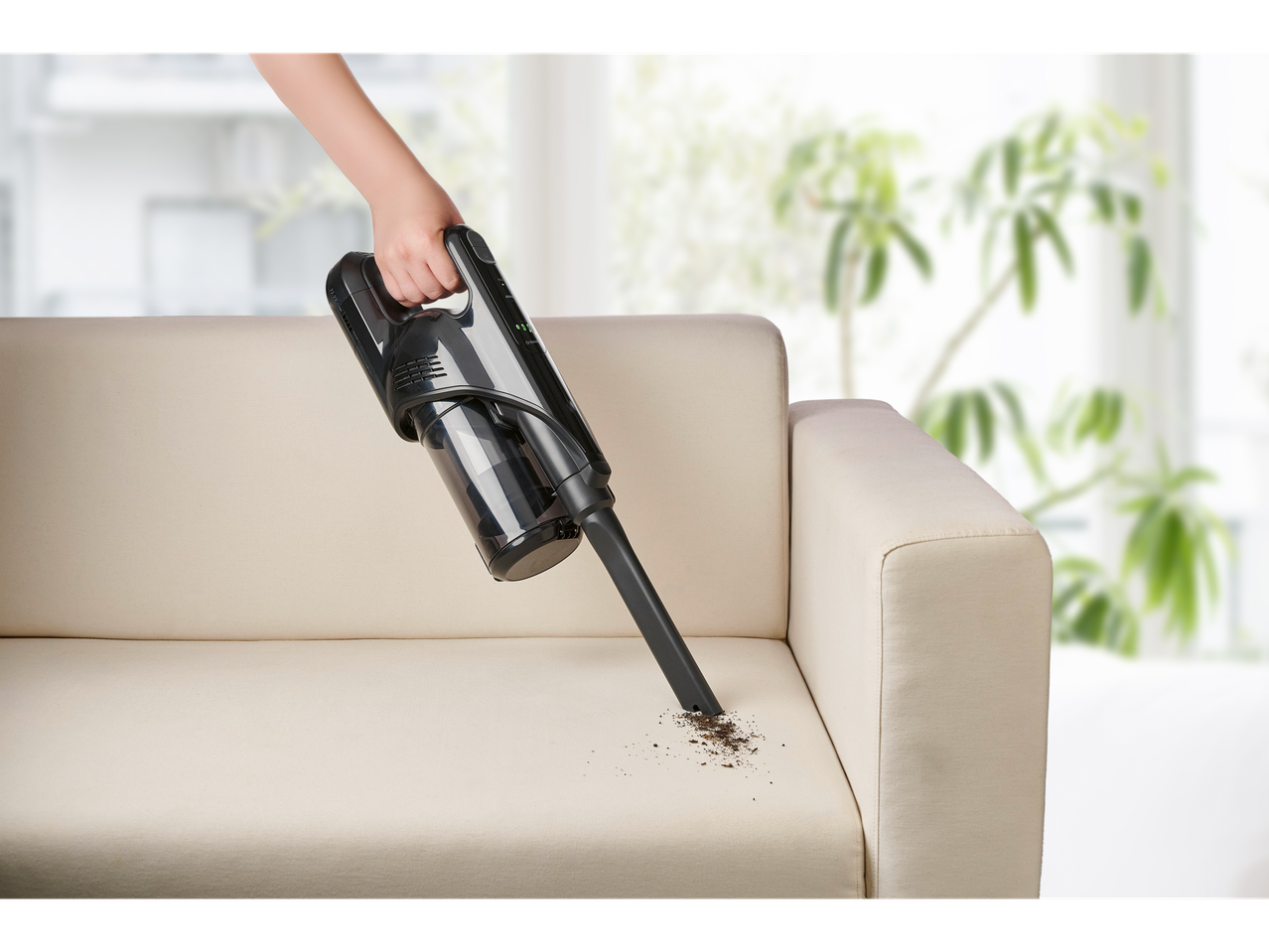 Aspirador de mão Silvercrest® 2 em 1 a limpar migalhas de um sofá bege.