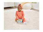 Happy baby in a coral outfit with white snowflakes playing with a light-up learning toy on a white rug.
