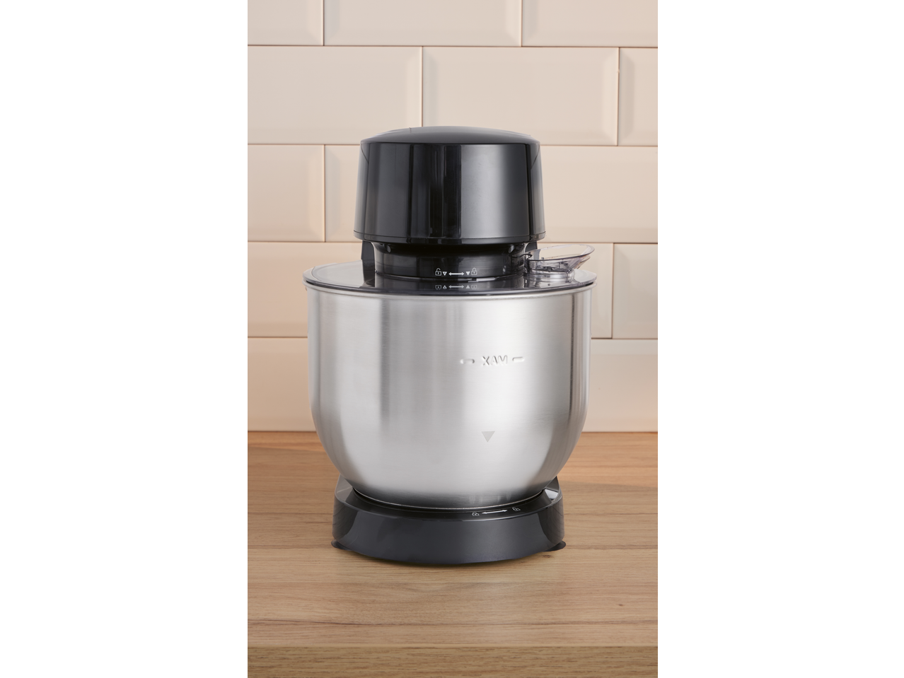 Robô de cozinha com tampa preta e taça de aço inoxidável sobre uma superfície de madeira.