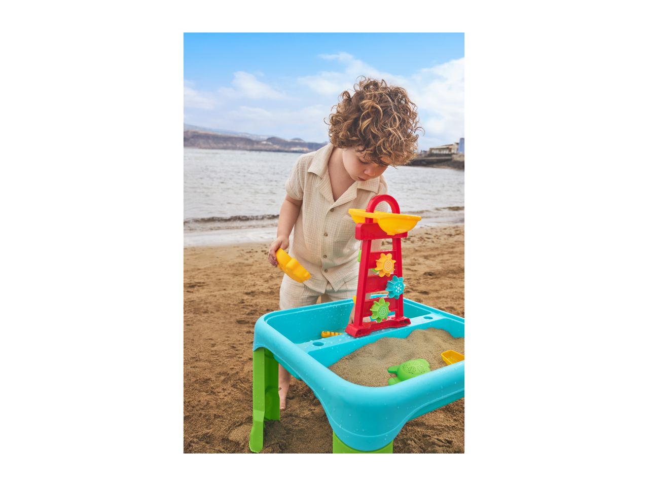 A child playing with a sand and water table on a beach.