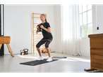 Mulher com roupa desportiva Crivit a fazer agachamentos com kettlebell num ginásio.