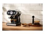 A black SilverCrest espresso machine brewing coffee into two glasses on a wooden counter.