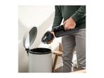 A person emptying a handheld vacuum cleaner into a trash can.