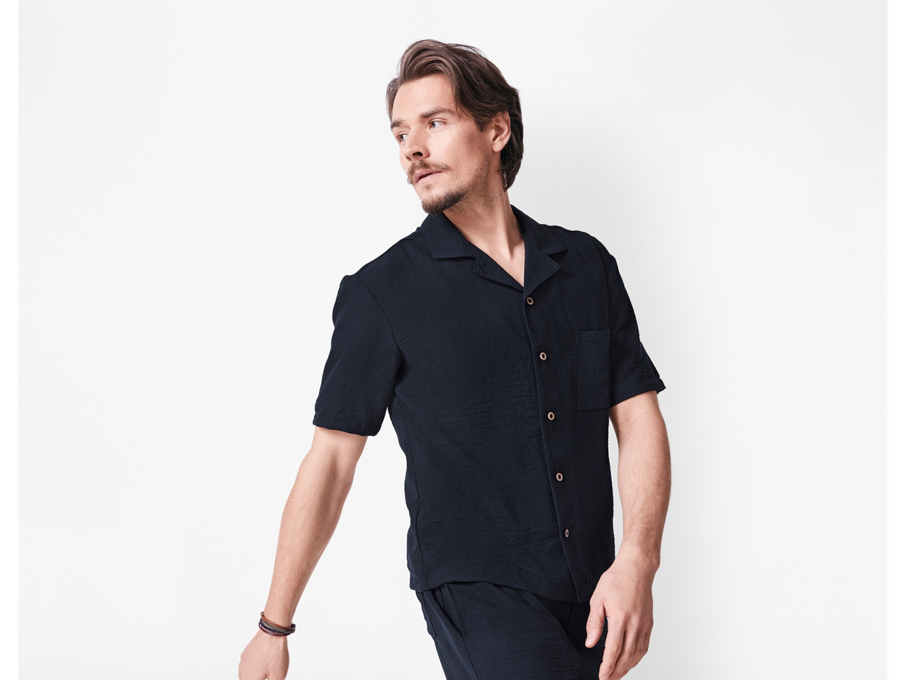 Model masculin îmbrăcat într-o cămașă și pantaloni scurți negri.