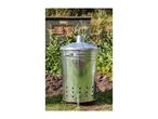 A galvanized steel compost bin sits in a garden amongst growing plants.