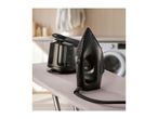 Black steam iron and water tank on an ironing board in a laundry room.