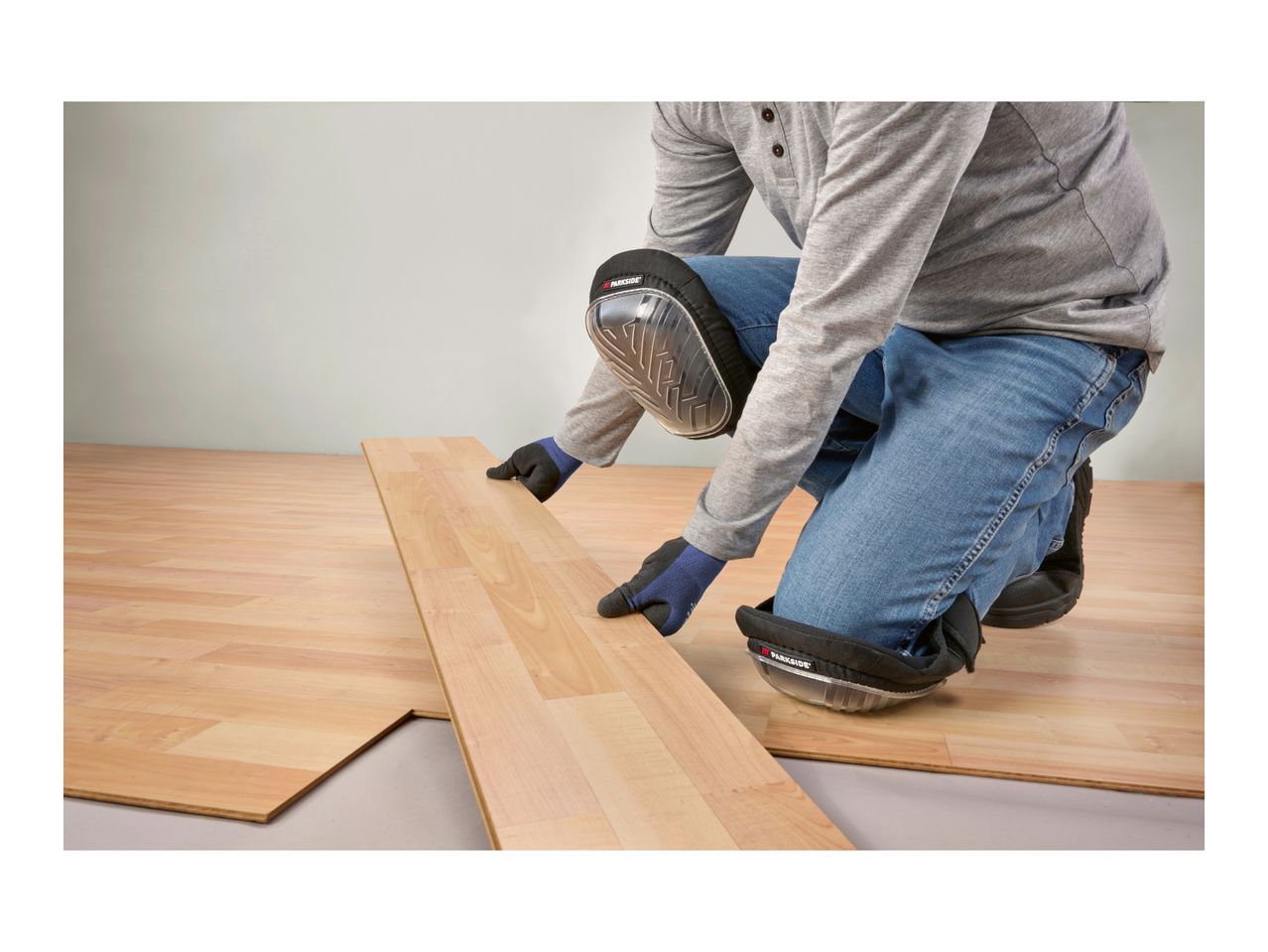 Person installing laminate flooring, wearing Parkside knee pads and work gloves.