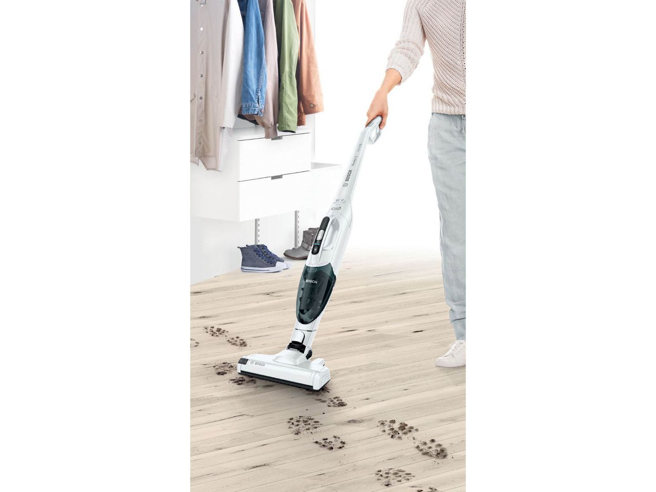 Una persona usa un aspirapolvere Bosch per pulire impronte di fango su un pavimento in legno.
