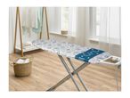 Ironing board with seashell pattern, laundry basket, and clothes rack in a bright room.