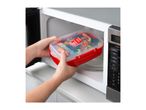 Hands placing a red microwave container filled with fresh vegetables into a microwave oven.