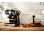 Máquina de café expresso a preparar café em duas chávenas, com biscoitos e grãos de café.